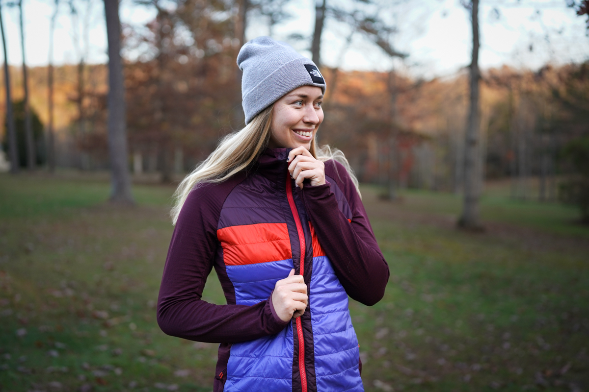 A woman zips up a warm jacket on a fall day in the woods.