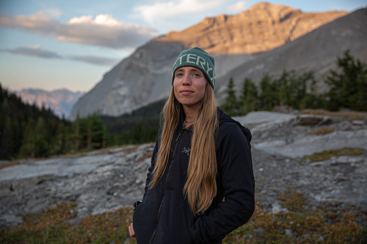 A woman stands in front of a sweeping mountain range