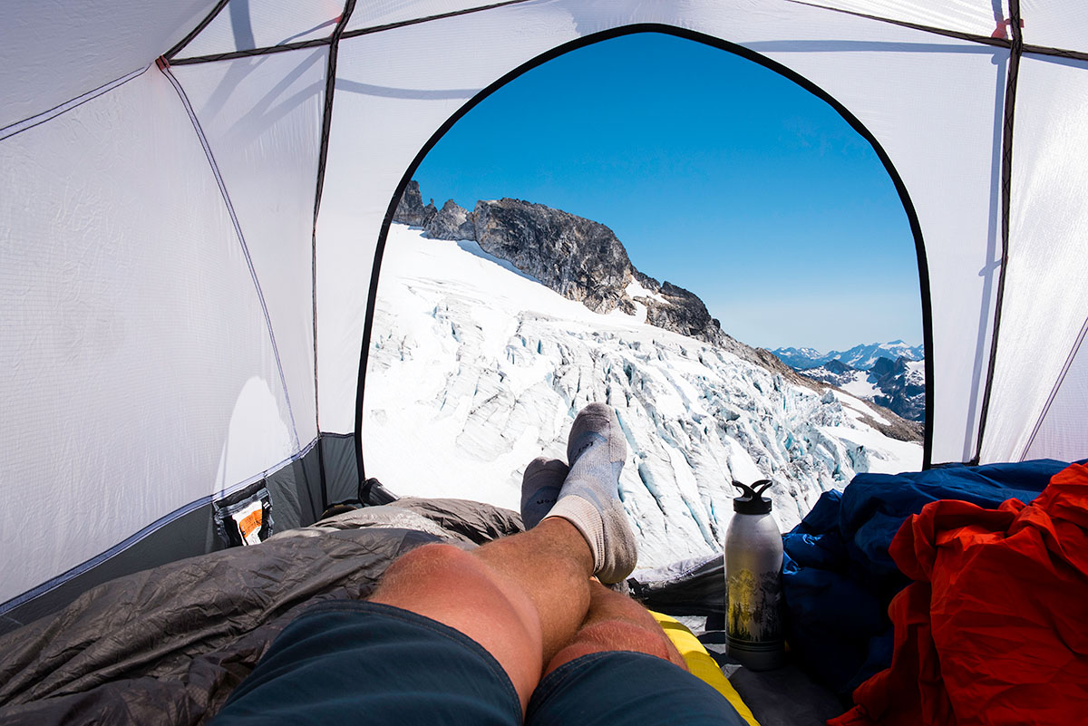 A man sitting with his feet hangin out of a tent on a glacier