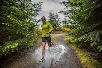 A woman runs through a muddy and wet dirt path in the forest.