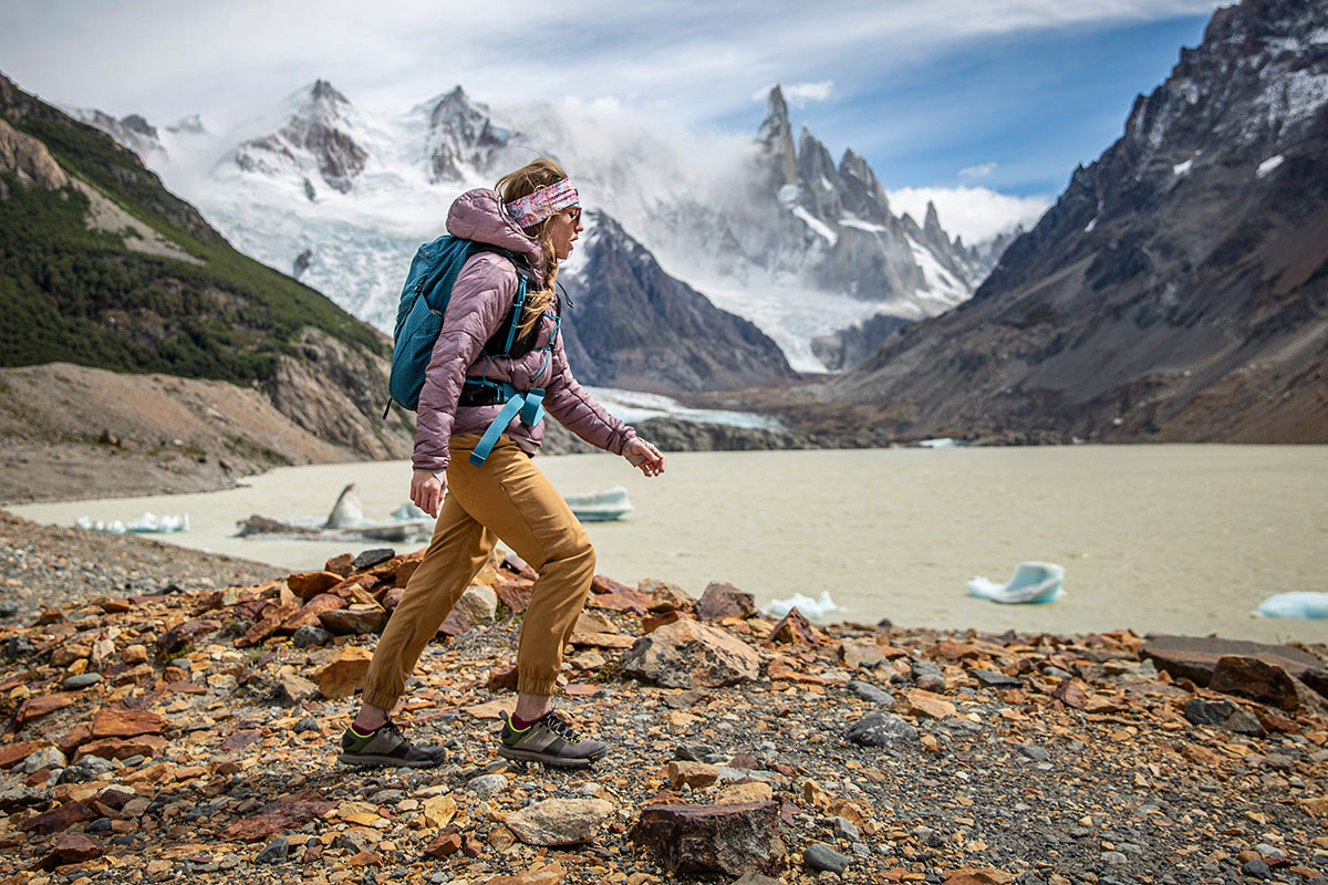 A woman hikes in front of mountains in Patagonia wearing a synthetic jacket.