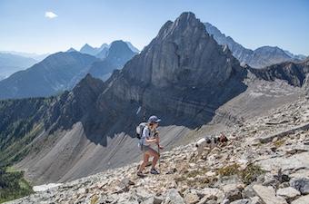 A woman hikes with her dog through a vast mountain valley