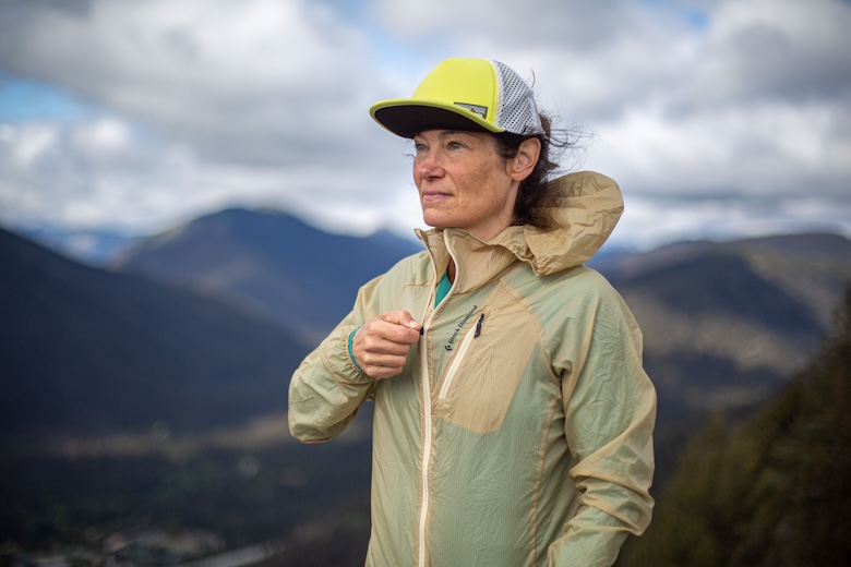 A woman zips up a windbreaker against strong mountain wind.