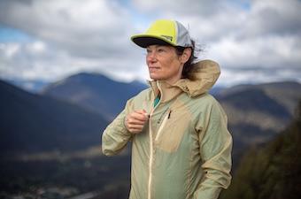 A woman zips up a windbreaker against strong mountain wind.