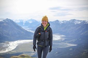 A woman wearing the Arc'teryx Cerium Hoody in the mountains smiles while hiking