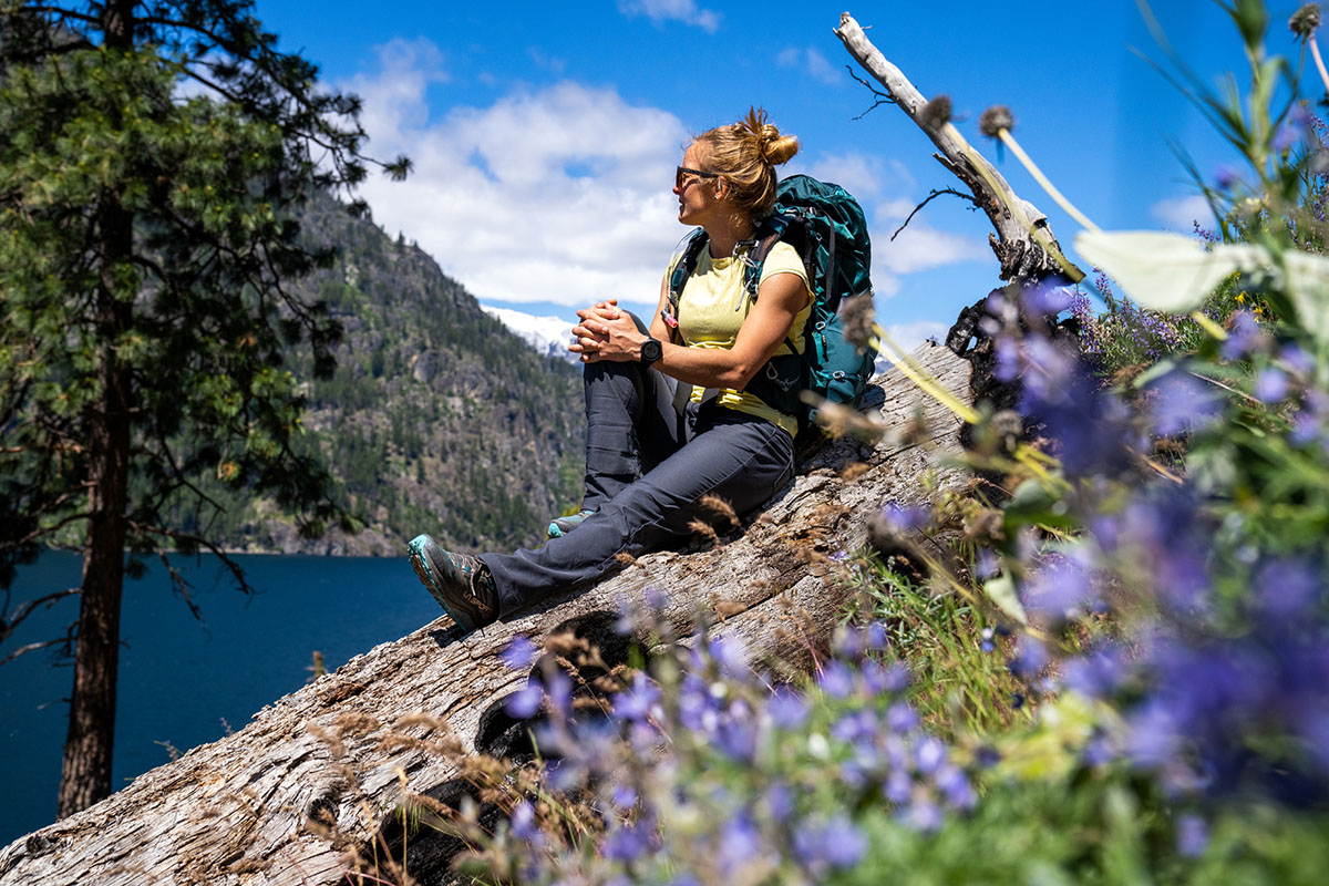 A hiker sits on a rock, taking in an alpine lake view on a sunny day.