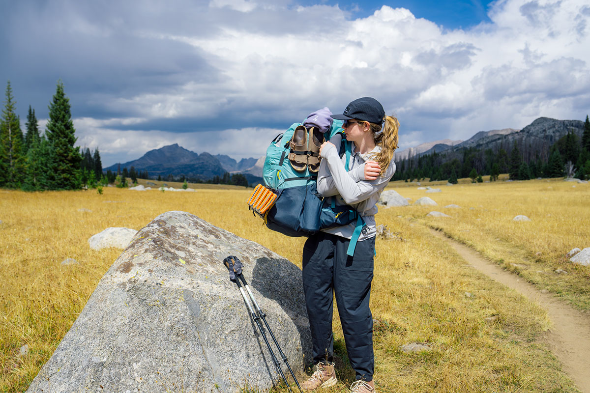 A hiker takes off their heavy backpack to set it on a rock.